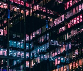 Windows of office blocks with workers sat in them at night